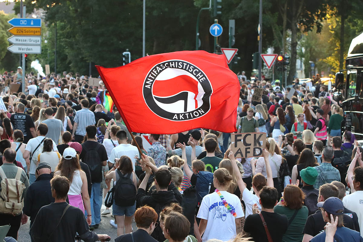 Das Fotos zeigt die vom betrachter wegziehende Demo mit einer großen Antifaschistische Aktion Fahne" und einer Texttafel mit dem Text: "FCK AfD" (Fick AfD)