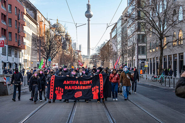 Das Transparent mit dem Text "Antifa bleibt Handarbeit" hinter dem viele Menschen laufen.Im Hintergrund ist der Berliner Fernsehturm zu sehen. 